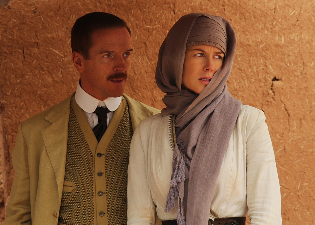 A man in a light suit is looking at a woman, but she is looking in the other direction. The woman is wearing a white top and a light purple headscarf.