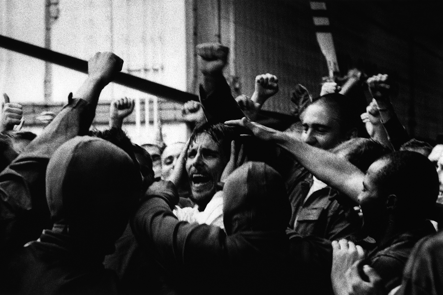 Black and white photo: A man is surrounded by many others. They seem to be cheering him on, grabbing him by the head.