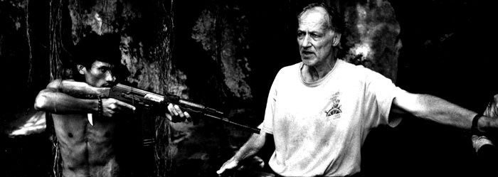 Black and white photo: On the left an actor holding a rifle on the trigger, on the right the director.