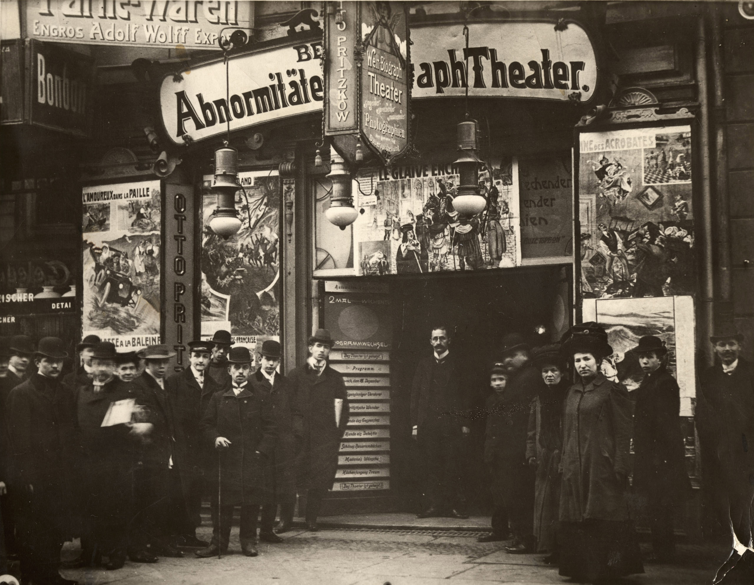 Schwarz-Weiß-Foto: Biograph-Besucher*innen vor der Fassade mit Filmplakaten