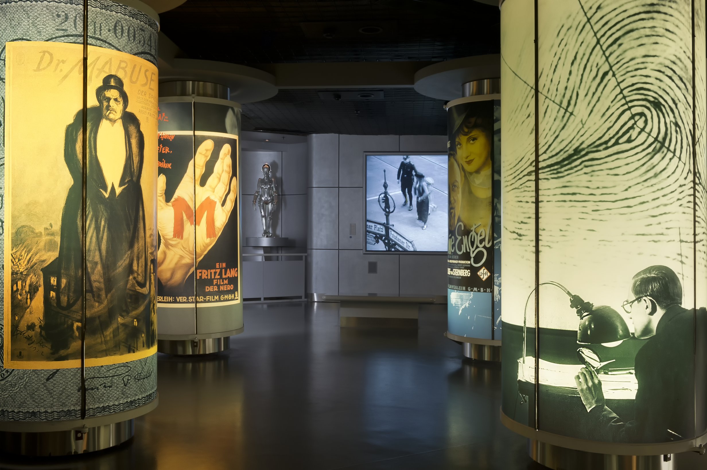 Blick in die ständige Ausstellung: Ein dunkler Raum mit angeleuchteten Plakaten und Fotos