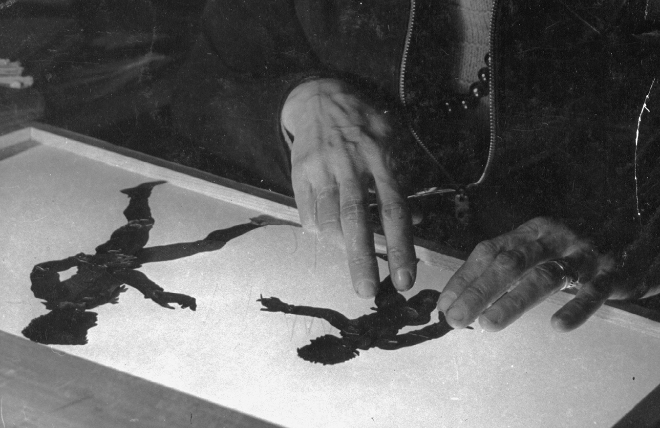 The hands of Lotte Reiniger are laying silhouette figures on an illuminated table.