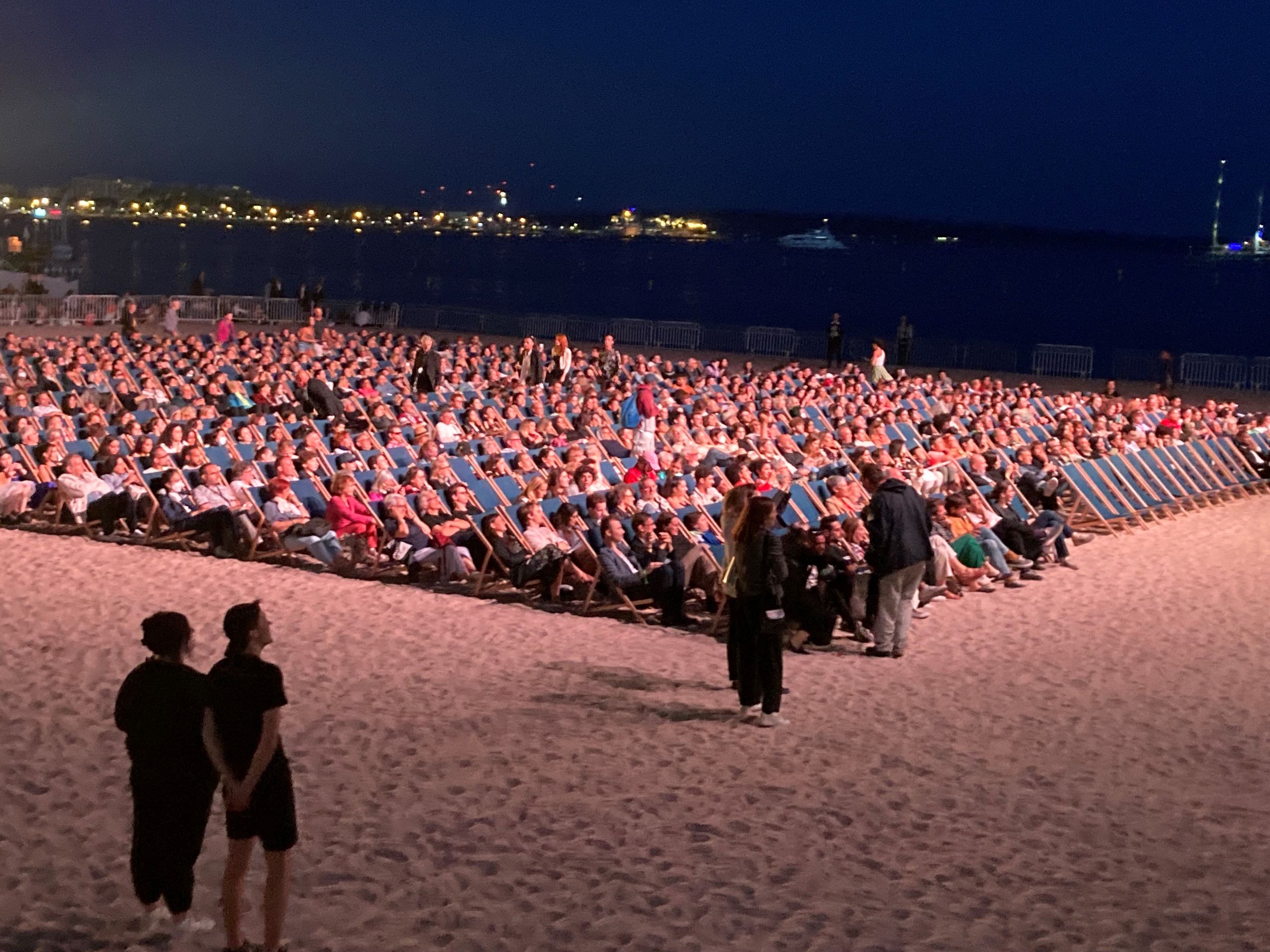 Eine Strand voller Menschen in Liegestühlen, ordentlich aufgereiht in eine Richtung positioniert 