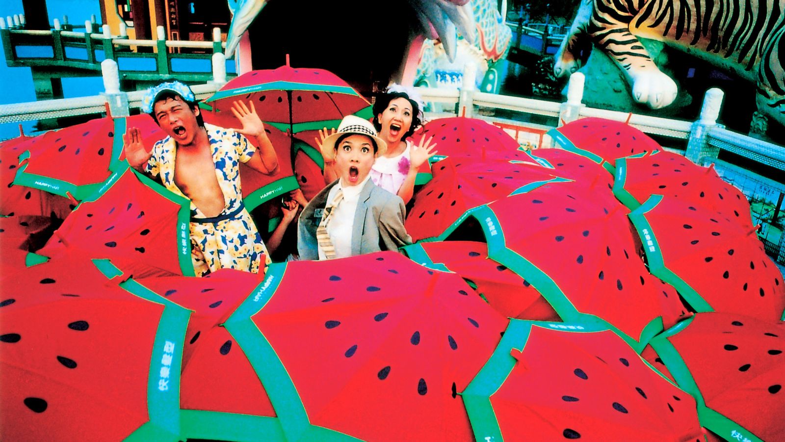 Zwei Frauen und ein Mann in einem Meer aus Regenschirmen mit Wassermelonen-Aufdruck