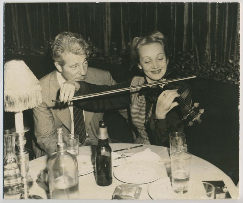 Marlene Dietrich playing the Violin next to Jean Gabin at a restaurant table