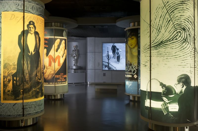 View of the exhibition: a dark room with illuminated posters.