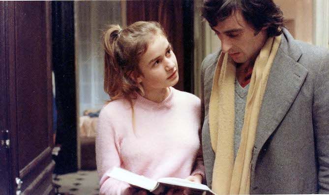 Ein junges Mädchen zeigt ihrem Vater ein Buch, der rechts neben ihr steht, und schaut ihn an.