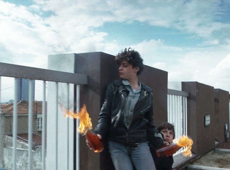 Ein Junge steht auf einer Brücke und hält zwei brennende Molotowcocktails in seiner Hand.