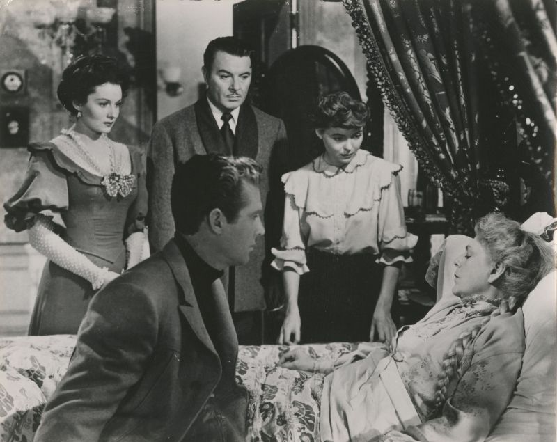 Zwei Frauen und zwei Männer am Bett einer älteren Dame mit langem Zopf.