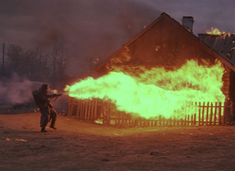 Soldaten stecken mit Flammenwerfern Holzhäuser in Brand.