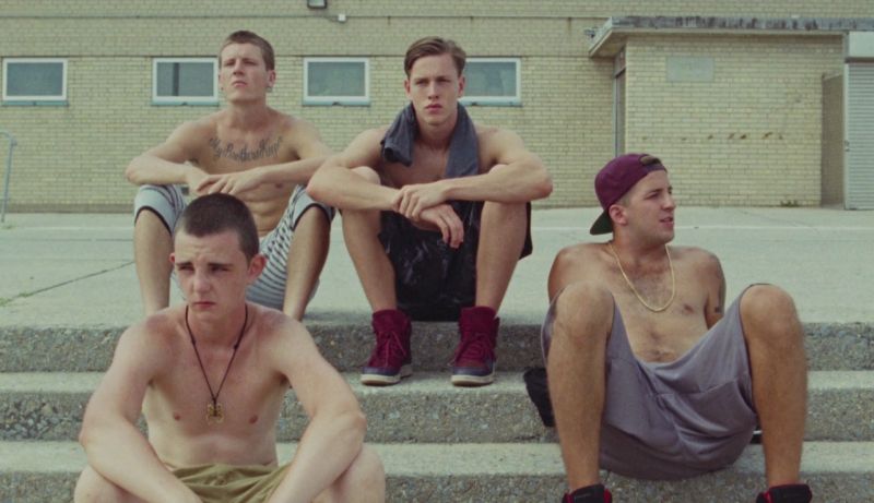 Vier Jungs mit nackten Oberkörpern sitzen auf einer Treppe und sehen missmutig aus.