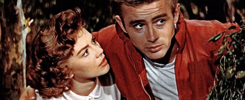 Still in color: Close-ip of a blond woman in the arm of a dark-haired man, looking at him while he faces the camera.