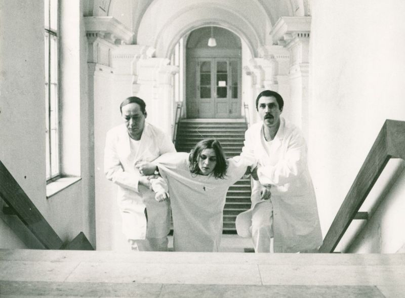 Eine Frau wird von zwei Männern in weißer Kleidung eine Treppe hochgezogen.