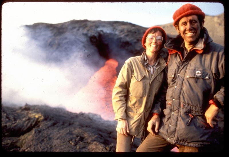 Die Vulkanolog*innen stehen Arm und Arm vor einem Lava-Strom.