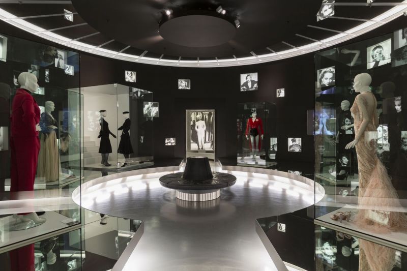 Kostüme und Fotos von Marlene Dietrich in einem runden Raum mit schwarzen Wänden.