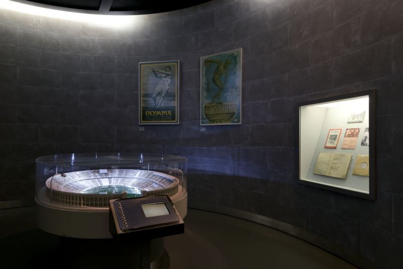 A dark room with a model of the  Olympia-stadium and posters on the wall.