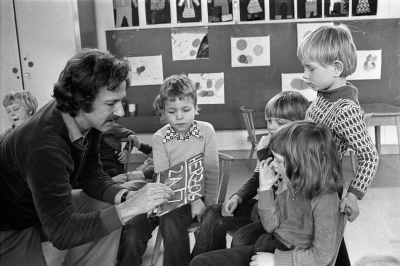 Werner Herzog kniet vor fünf Kindern und schreibt mit Kreide etwas auf eine kleine Tafel.