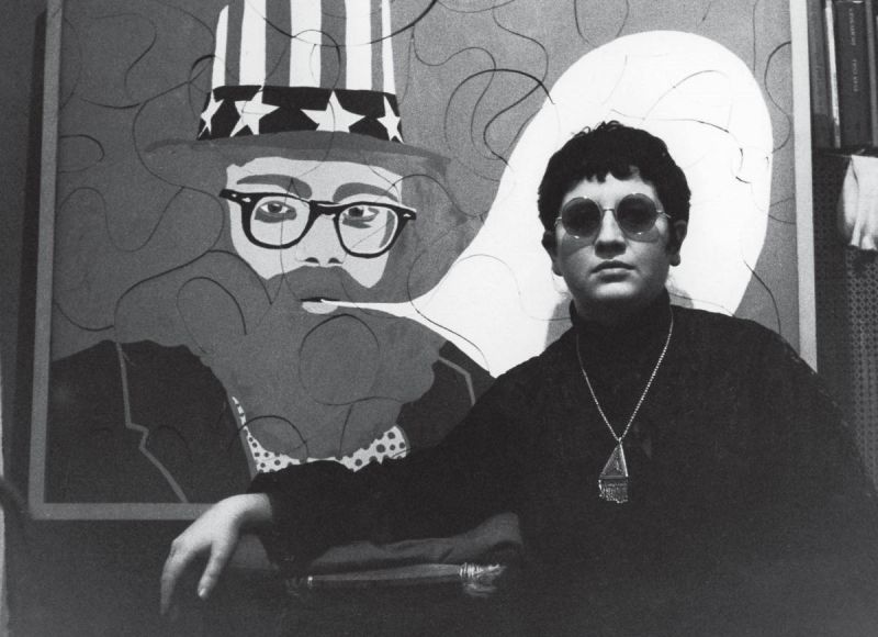 Schwarz-weiß Foto: Die Regisseurin vor einem Gemälde von Alan Ginsberg.