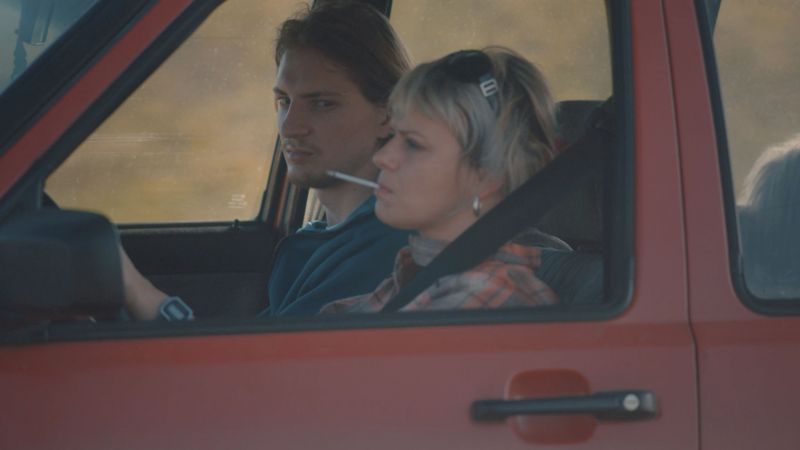 Woman and a man in a car, she is driving and smoking