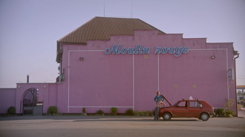 A red car parked in front of a pink building