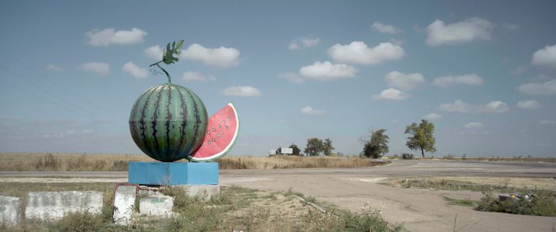Landschaft mit einer Skulptur in Form einer riesigen Wassermelone, die neben der Straße steht.