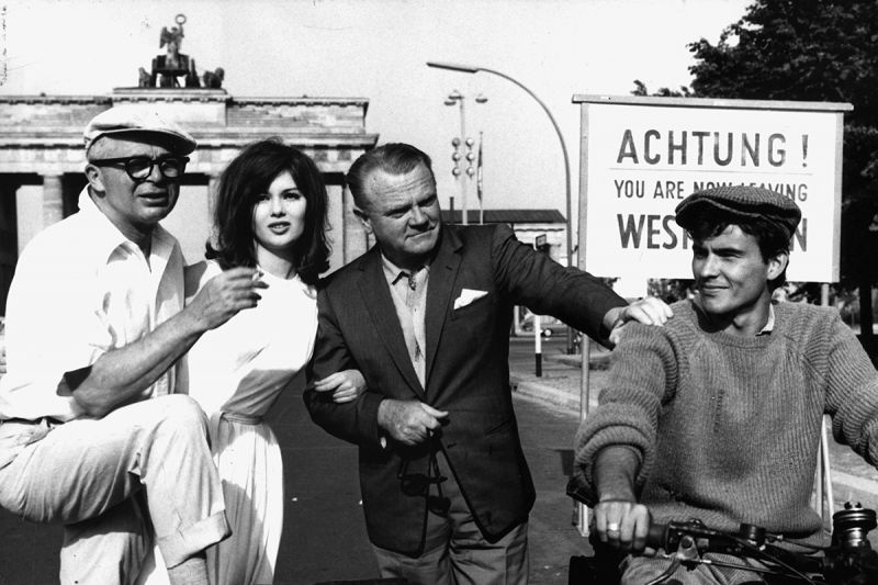 Schwarzweißfotografie von Regisseur Billy Wilder mit einer Schauspielerin und zwei Schauspielern vor dem Brandenburger Tor