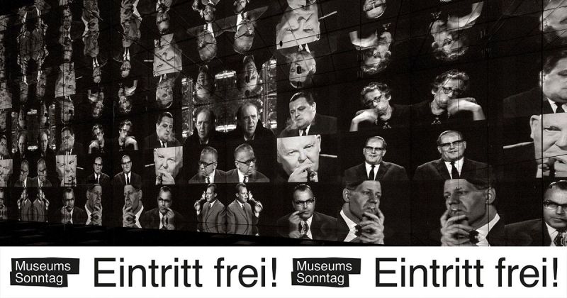 Bildschirmwand mit vielen Gesichtern und dem Sticker "Museumssonntag – Eintritt frei!" 