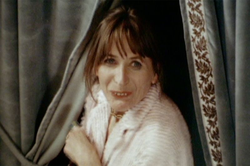 Eine Frau in einer hellen Bluse blickt durch einen grauen Vorhang.