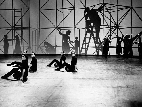 Black and white still from Portraits in Musik: dance troupe, dressed in black, perform in front of some scaffolding in a studio