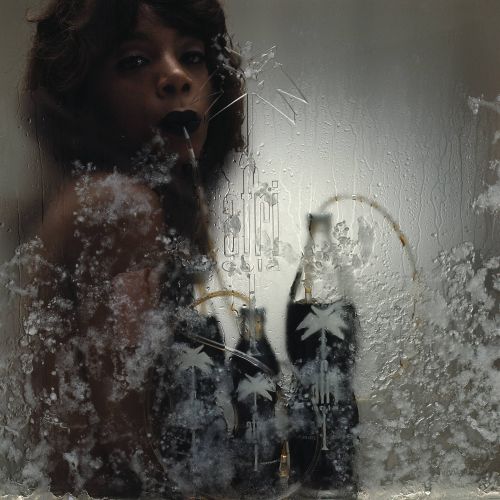 Commercial still: dark-haired woman leans against a frozen glass panel with the brandname "Afri-Cola" on it