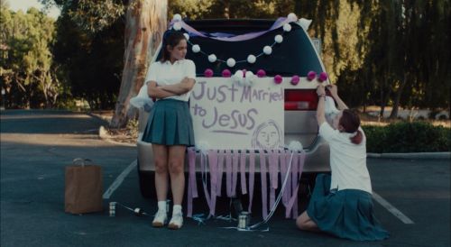 Zwei Mädchen auf einem Parkplatz, zwischen ihnen ein Auto mit der Aufschrift: Just married to Jesus.