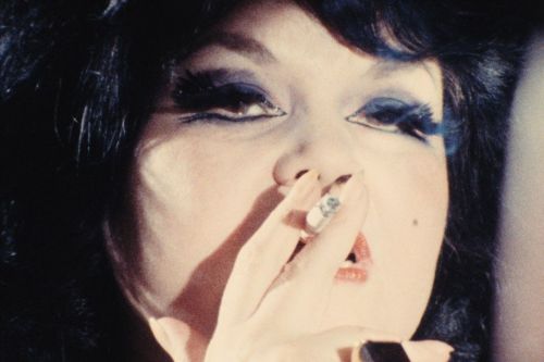 Close-up of a dark-haired woman with dark eye make-up smoking a cigarette.