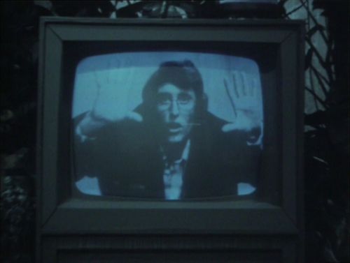 An old television set which shows a man holding out his hands and talking as if explaning something to the audience.