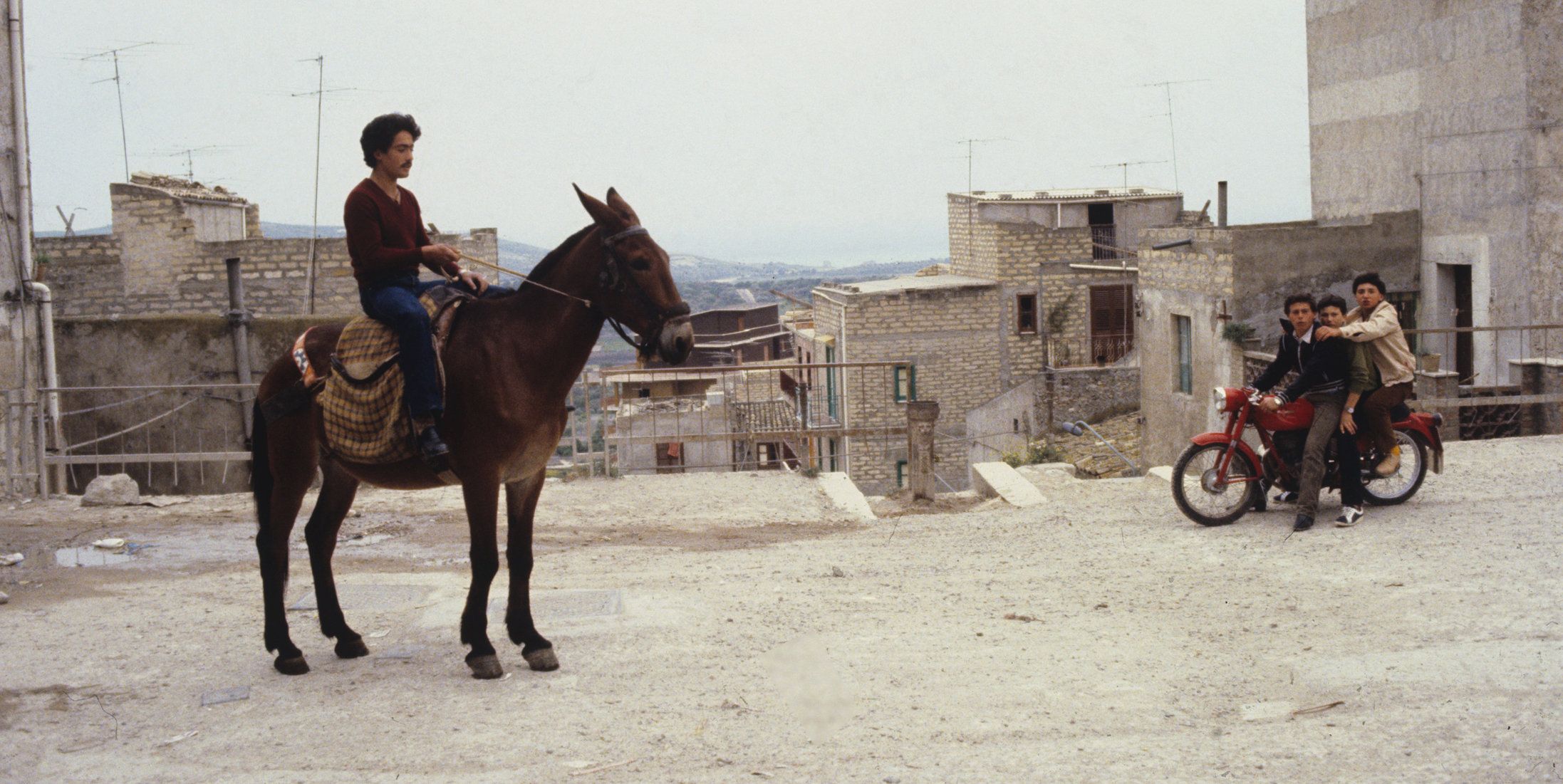 Farbiges Szenenfoto: Ein Mann sitzt auf einem Pferd, im Hintergrund eine heruntergekommene Stadt