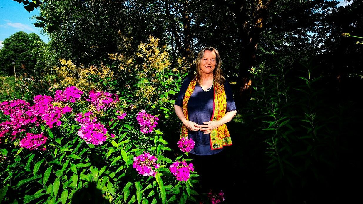Die Regisseurin steht draußen neben einem Busch mit pinken Blumen