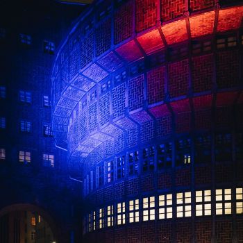 Das Vordergebäude der Kinemathek, ein Klinkerbau, wird in mehreren Farben angeleuchtet, während Menschen davorstehen.