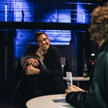 Zwei Menschen umarmen sich, umgeben von Stehtischen.