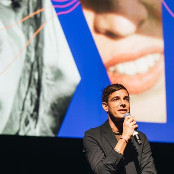 Ein Mann steht mit einem Mikrofon vor einer Leinwand.