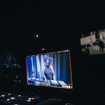 Eine Frau mischt auf einem Bildschirm Musik und dahinter ist eine Leinwand mit Schwarzweißbildern.