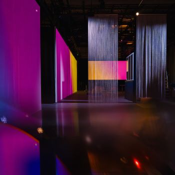 Eine gro&szlig;e Halle mit Projektionsfl&auml;chen, auf die pinke und orangene Farbfl&auml;chen projiziert werden.