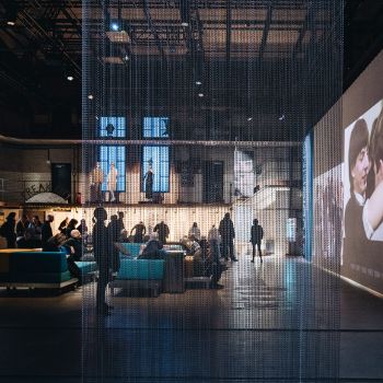 Viele Menschen in einer Industriehalle mit moderner Inszenierung und gro&szlig;er Bildschirmwand.