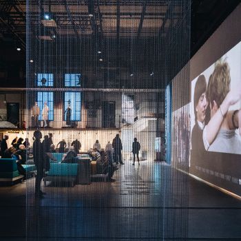 Viele Menschen in einer Industriehalle mit moderner Inszenierung und gro&szlig;er Bildschirmwand.
