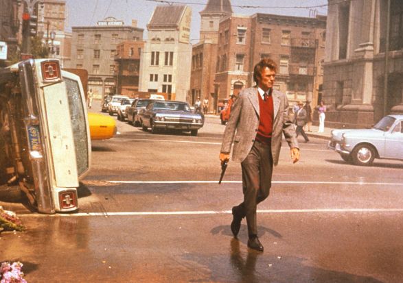 Der Schauspieler Clint Eastwood l&auml;uft &uuml;ber eine Stra&szlig;e, neben ihm liegt ein umgedrehtes Auto. The actor Clint Eastwood walks across a street, next to him is an overturned car.