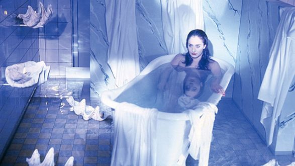 Frau h&auml;lt einen Mann in einer Badewanne fest, w&auml;hrend Wasser spritzt.