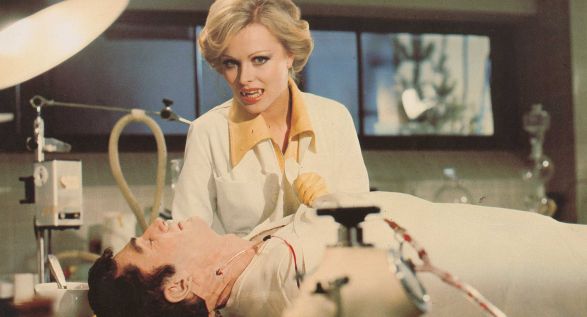 Ein Frau mit blonden Haaren und Vampirz&auml;hnen beugt sich &uuml;ber einen bewusstlosen Mann, der auf einer Bahre liegt und dem Blut entnommen wird.