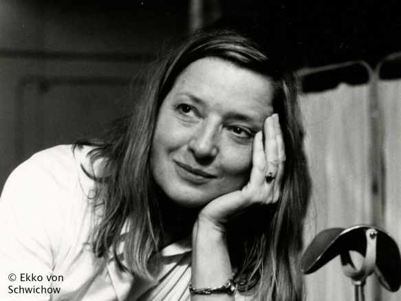 Eine Frau sitzt, den Kopf in die Hand gestützt. Sie lächelt.