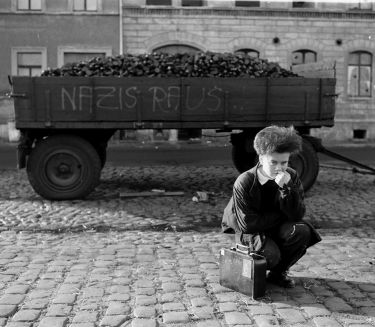 Ein kleiner Junge kniet vor einem Wagen, auf den die Worte Nazis raus gemalt sind.