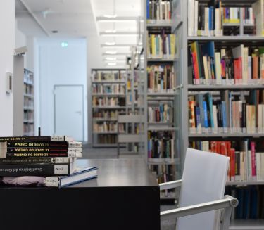 In einem Raum mit vielen Regalen voller Filmb&uuml;cher stehen ein Tisch und ein Stuhl und auf dem Tisch liegen weitere Filmb&uuml;cher.