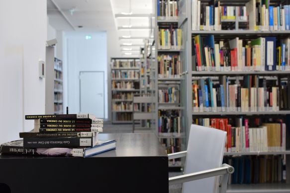 In einem Raum mit vielen Regalen voller Filmbücher stehen ein Tisch und ein Stuhl und auf dem Tisch liegen weitere Filmbücher.