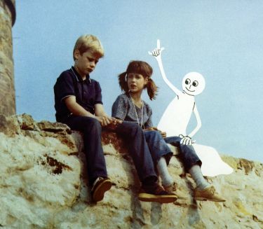 Zwei Kinder sitzen auf einer Mauer und unterhalten sich, daneben sitzt ein Zeichentrick-Gespenst und meldet sich.